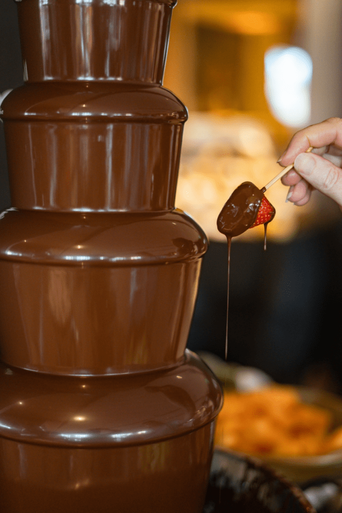Hand dipping fruit into a flowing chocolate fountain.